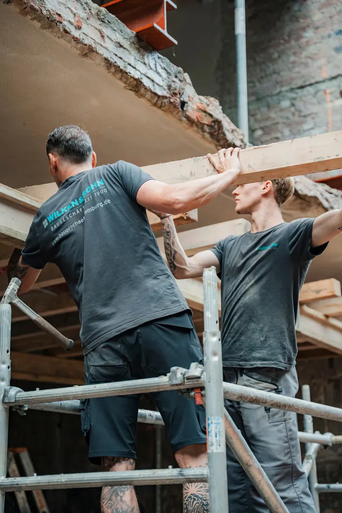 Handwerker tragen einen Holzbalken auf dem Gerüst